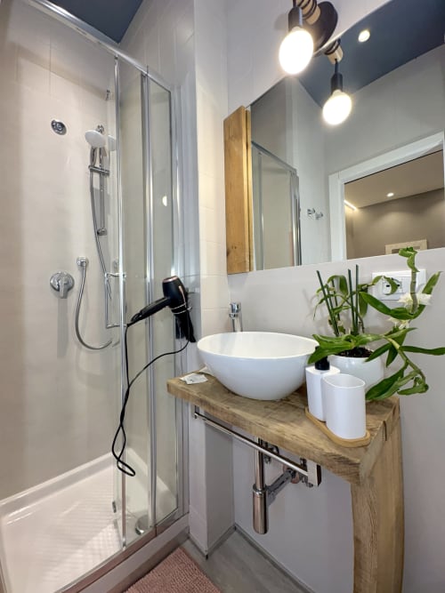 Bagno moderno presso l'appartamento Le Arche a Verona con doccia, lavabo bianco su mobiletto in legno e pianta in vaso