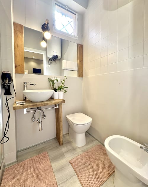 Moderno bagno dell'appartamento Le Arche Verona con lavabo rotondo bianco, mobile in legno, wc, bidet, vasca e piastrelle
