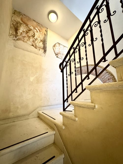Scala con ringhiera in ferro battuto nero nell'appartamento Le Arche di Verona, con pareti color crema e soffitto arrotondato