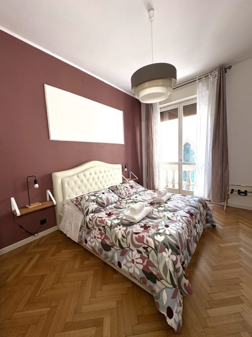 Elegante camera da letto presso Le Arche B&B a Verona con pareti bordeaux, testata capitonnée color crema, biancheria floreale e vista città