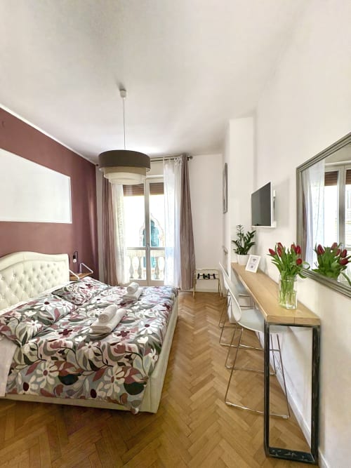 Camera moderna dell'Hotel Le Arche a Verona con parete accent bordeaux, biancheria floreale e balcone con vista sulla città