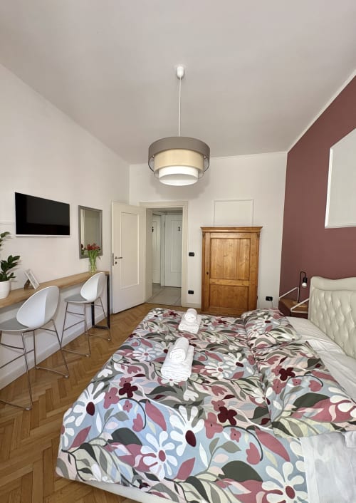 Camera moderna dell'Il Tenore B&B a Verona con biancheria floreale, scrivania, mobili in legno e illuminazione a sospensione