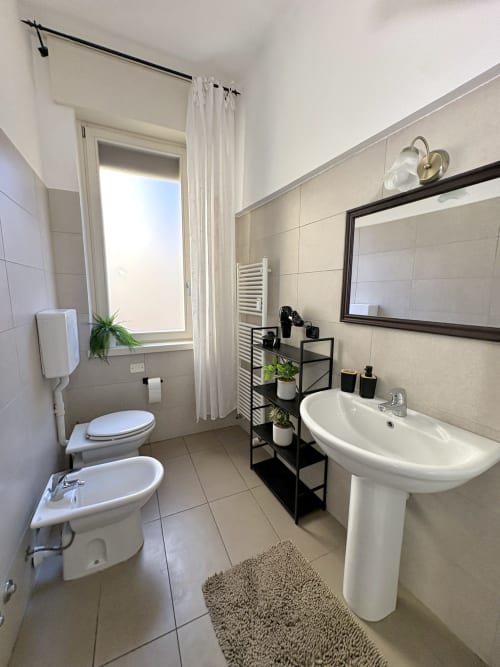 Bagno moderno dell'Hotel Le Arche a Verona con lavabo su colonna, toilette, bidet e mobile nero con piante