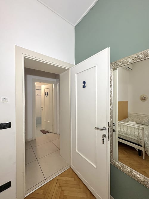 Ingresso della camera Rigoletto al Le Arche B&B di Verona con porte bianche, pavimento piastrellato e motivo a spina di pesce in legno