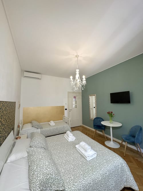 Camera moderna Le Arche Verona con due letti, lampadario in cristallo, parete accent verde salvia, pavimento in legno e TV