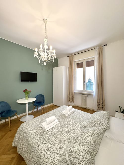 Elegante camera da letto presso l'Il Tenore B&B Rigoletto a Verona con parete verde salvia, lampadario in cristallo, letto matrimoniale e vista sulla città
