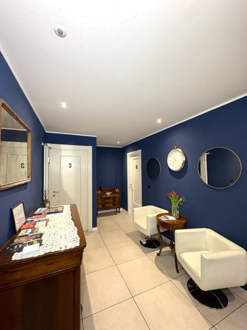 Area reception moderna della struttura Le Arche B&B Verona con pareti blu scuro, soffitto bianco, banco ricevimento, sedute e specchi