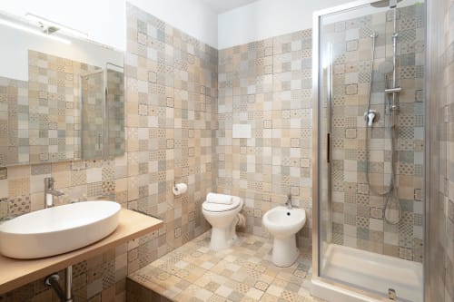Bagno moderno dell'appartamento IV House Rome con piastrelle decorate, lavabo rotondo, wc, bidet e doccia con box in vetro