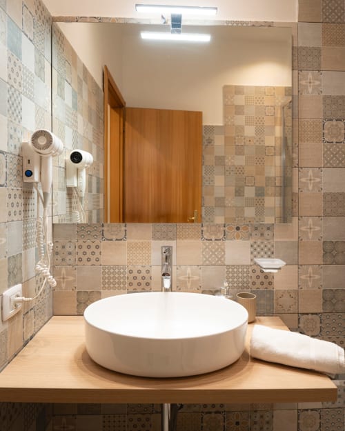 Bagno moderno dell'appartamento IV House Roma con lavabo rotondo bianco, piastrelle decorative e vanity in legno