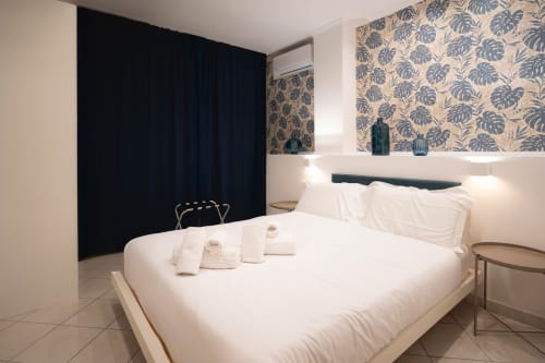 Camera da letto moderna con letto bianco, carta da parati tropicale, tende scure e arredamento contemporaneo presso IV House Roma