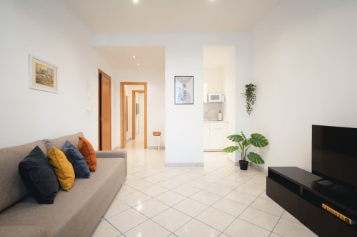 Moderna sala da soggiorno a Roma con divano grigio, TV, zona pranzo e piante verdi presso IV House B&B
