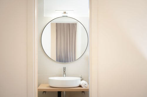 Vanity moderna del bagno a IV House Roma con specchio rotondo, lavandino in ceramica bianca e piano in legno