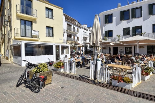 Beachfront apartment terrace in Palafrugell with seaside dining, white railings, umbrellas, and Mediterranean architecture
