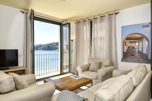Seafront apartment living room in Palafrugell with sea views, cream furnishings, wooden table, and balcony access to