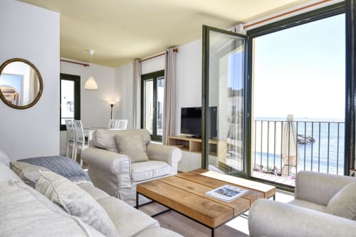 Bright seafront apartment in Palafrugell with beige furniture, wooden table, TV, and balcony overlooking the sea