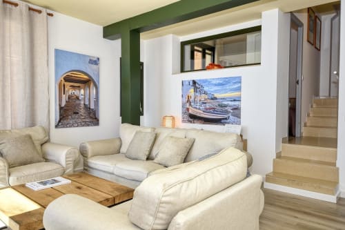 Bright seafront apartment living room in Palafrugell with cream sofas, wooden floors, green accents, and coastal artwork