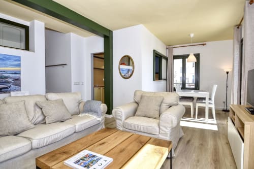 Bright seafront apartment living room in Palafrugell with cream furniture, wooden floors, kitchenette, and sea views through