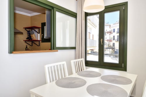 Bright dining room with white table, striped chairs, green-framed windows overlooking Palafrugell seafront apartment