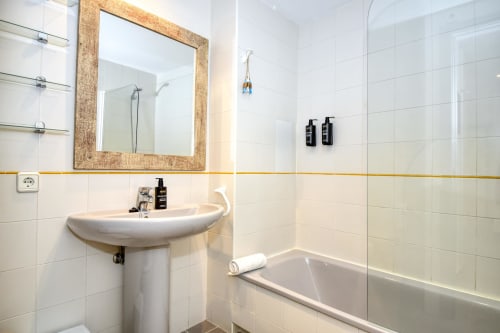 Modern bathroom with pedestal sink, framed mirror, white tiles, bathtub, and glass shower enclosure in seafront apartment,