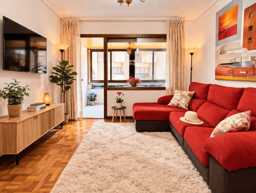 Amplio apartamento Breixo en Baiona con sofá rojo, muebles de madera y balcón con vistas a la ciudad