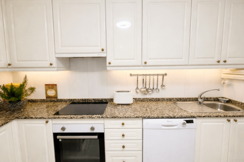 Cocina moderna blanca con encimeras de granito, electrodomésticos de acero inoxidable y herrajes de latón en el apartamento Amieiro, Baiona