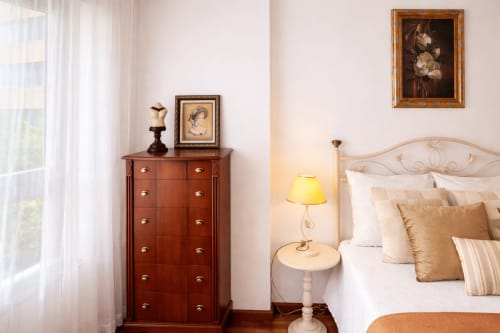 Elegante dormitorio del apartamento Amieiro de Holibai en Baiona - cómoda de madera, obras de arte enmarcadas, cama con cojines decorativos, mesita de noche