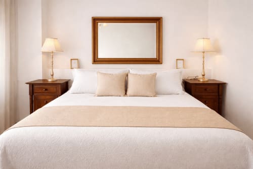 Elegante dormitorio en apartamento Holibai, Baiona con cama queen, mesitas de madera, lámparas y espejo con marco sobre cabecera