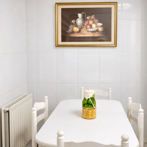 Elegante comedor en apartamento de Baiona con mesa blanca, bodegón de frutas enmarcado y radiador