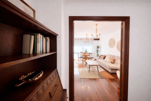 Puerta de madera que abre al luminoso salón del apartamento Amieiro en Baiona, con sofá crema, lámpara de araña y suelos de madera