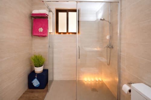 Moderno plato de ducha con puertas de cristal en la casita Holibai de Baiona, con iluminación decorativa, toallas rosas y maceta