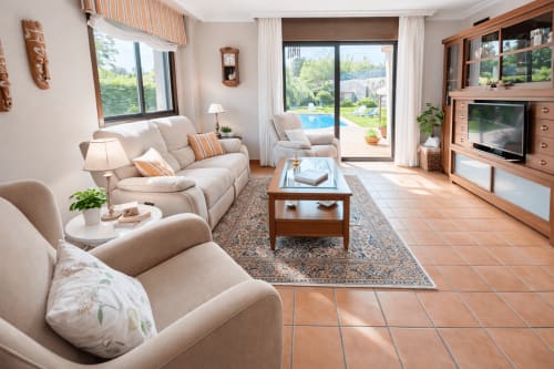 Luminoso salón con sofás crema, muebles de madera y puertas de cristal al jardín y piscina de Holibai en Baiona