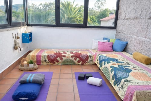 Sala de yoga en la cabaña Holibai de Baiona con colchonetas púrpuras, ropa de cama colorida y vistas a la montaña desde grandes ventanales