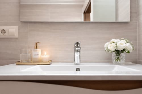 Moderno lavamanos en la casa rural Holibai de Baiona con lavabo blanco, grifo cromado y flores frescas en jarrón decorativo