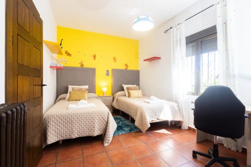Bright twin bedroom at Finca Navalpino with yellow accent wall, terracotta floors, and modern furnishings in Guadamur.