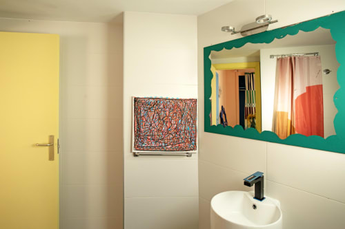 Baño moderno colorido con puerta amarilla, espejo con marco ondulado verde y obra de arte abstracta en el hotel Formentera Especial