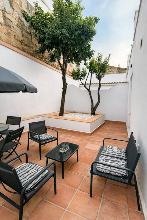 Área de descanso en patio con sillas negras, muros blancos y árboles del apartamento Wehost Costaluz Puerto Santa María