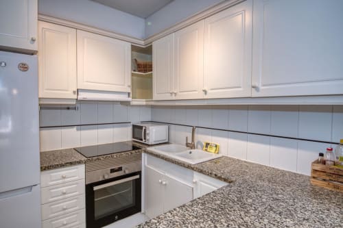 Modern kitchen with white cabinets, granite countertops, stainless steel appliances in beachfront apartment, Palafrugell