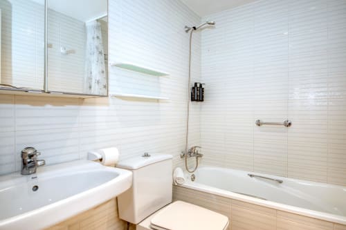 Modern bathroom with white tile walls, sink, toilet, bathtub with shower, and mirror at beachfront apartment in Palafrugell