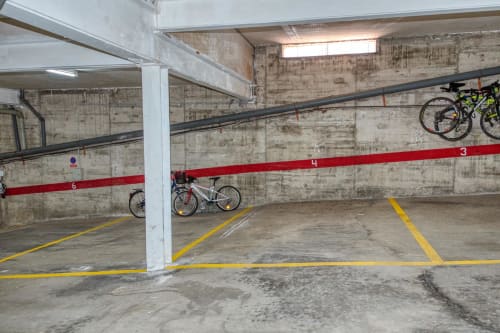 Underground parking garage with numbered spaces, bikes stored on wall, concrete floor with yellow lines at Finques Garcia