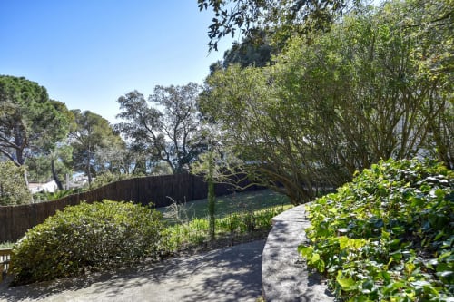 Allée paysagée de l'hôtel Finques Garcia Enrich à Palafrugell, bordée de verdure luxuriante et de clôture en bois