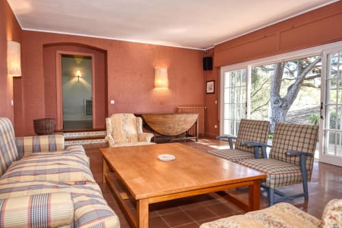 Salon chaleureux en terre cuite avec fauteuils rayés, table basse en bois et portes vitrées donnant sur les arbres à Finques Garcia