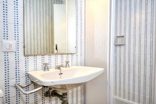 Salle de bain moderne avec carrelage bleu patterné, lavabo blanc et miroir à l'hôtel Finques Garcia Enrich de Palafrugell