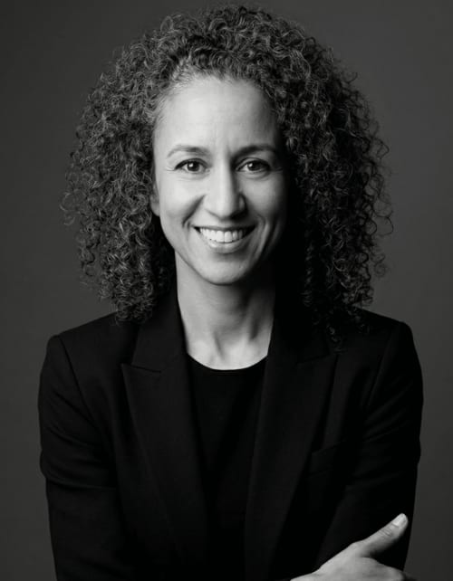 Retrato profesional de una mujer con cabello rizado sonriendo, vistiendo un blazer negro