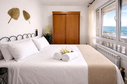 Dormitorio de lujo en Vila Natercia, Baiona, con vistas al mar, ropa de cama blanca, armario de madera y vista al océano