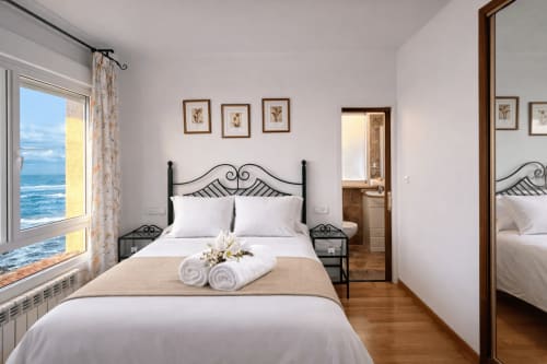 Elegante dormitorio con vistas al mar en Vila Natercia, Baiona con cama de hierro forjado, sábanas blancas y vistas al océano