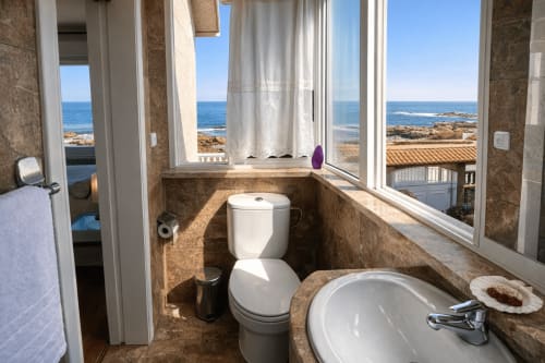 Baño costero en Vila Natercia, Baiona con vistas al mar por las ventanas, accesorios blancos y paredes con azulejos de terracota