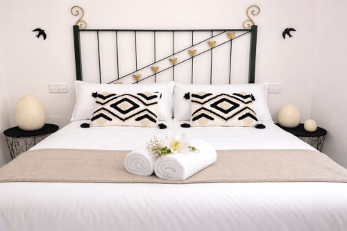Dormitorio moderno en Vila Natercia con cabecero de hierro forjado, almohadas con patrón geométrico, toallas enrolladas y vistas al mar