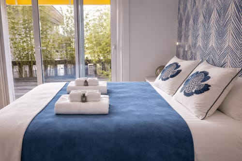 Dormitorio moderno con pasillo azul, almohadas blancas con patrones azul marino, toallas enrolladas, balcón con vista al mar, persianas amarillas, Panxón