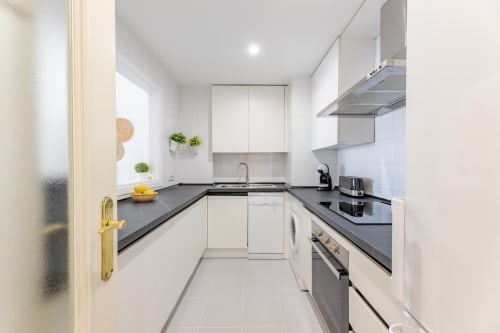 Modern white kitchen with dark countertops, stainless steel appliances, and window in Marbella apartment