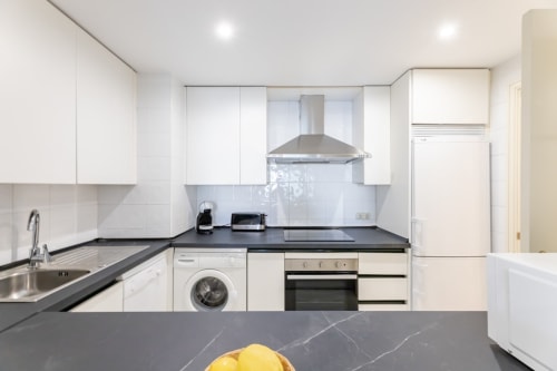 Modern white kitchen with dark countertops, stainless steel appliances, and range hood in Marbella apartment